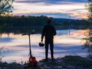 Young male rider on an electric scooter at sunset back view. Colorful landscape. Modern urban...