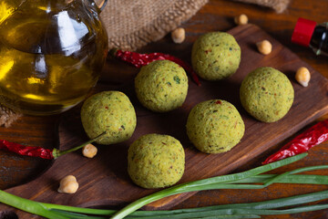 Close up with raw falafel on brown wooden board. Healthy vegetarian food, fitness eating. Falafel indredients on rustic kitchen. Jewish cuisine. Red chili pepper, green onions and chickpea