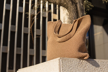 Plakat Brown knitted handmade bag on light stone pedestal on the street. Hero view. Eco-friendly shopping. Zero waste lifestyle.