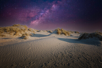 Night image of dune landscape with starry sky with purple and violet starlight against dark blue sky background