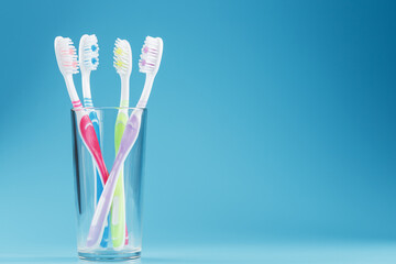 Toothbrushes of different colors in a transparent glass on a blue background.