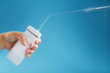 Irrigator in hand for cleaning the mouth with a shot of water jet on a blue background