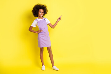 Full size photo of optimistic cute curly girl point empty space wear white t-shirt violet dress isolated on yellow color background