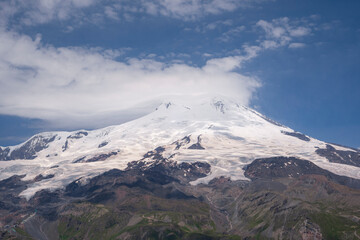 Volcano Elbrus. Its top is covered with clouds. They appeared in the afternoon. Landscape view in the south-east of mount from Cheget mount. Kabardino-Balkaria region, Russia.