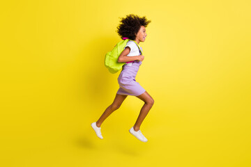 Fototapeta na wymiar Full length body size profile side view of cheerful wavy-haired girl jumping running to lesson isolated over bright yellow color background