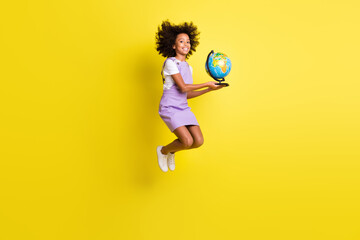 Full length body size view of cheerful wavy-haired girl jumping holding globe planet isolated over shine yellow color background