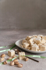 Pistachios halvah in plate with pistachios nuts with green ribbon on gray background, selective focus, vertical, copy space. This kind of halva is also known as 