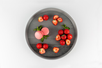 pink strawberry macaroni cakes on a gray plate with strawberries and mint leaves on a white background
