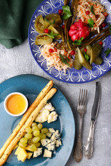 Assorted different types of cheese with grapes, honey and bread and plate of Assorted Pickled vegetables top view