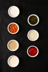 Bowls of various sauces on black background top view. set of sauces