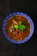 soup with beans and meat in bowl on dark background top view