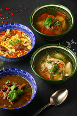 Set of four soups from worldwide cuisines, healthy food on dark concrete table.