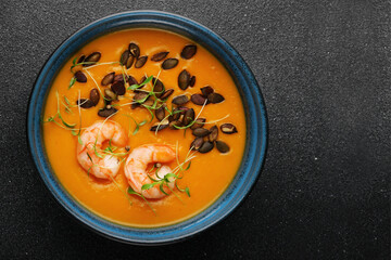 pumpkin cream soup with seeds and shrimps on dark concrete background and microgreen top view