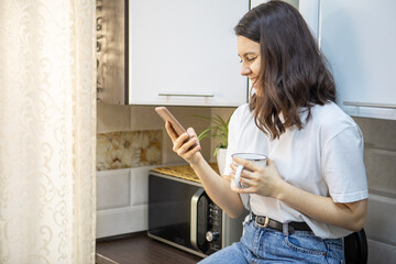 woman drinking morning coffee tea at the kitchen surfing internet on the phone