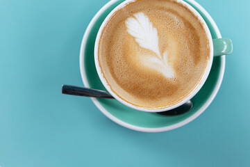 A hot latte in a green ceramic cup on a tone on tone blue turquoise background
