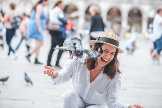 woman in white clothes with straw hat having fun with pigeons at venice city square