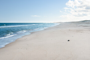 Large sandy beach backed by dunes on a clear autumn day. People strooling along the beach are visible in distance. 