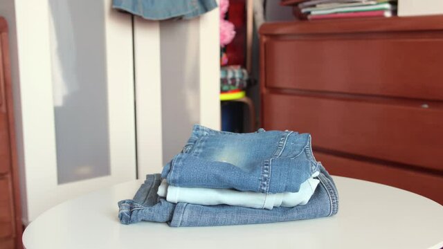 Vintage jeans being piled up on a table. Reusable clothes, eco friendly. A hand is putting jeans down one by one. 4K professional footage.