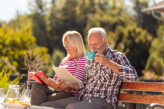 Senior couple drinking morning coffee and reading in the backyard - Powered by Adobe