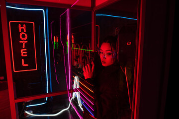 armed asian woman in sunglasses holding gun near neon hotel sign