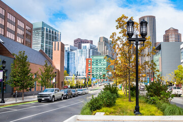 View of Boston Financial district skyline on a partly cloudy autumn day. Street lights and autumn trees are in foreground.