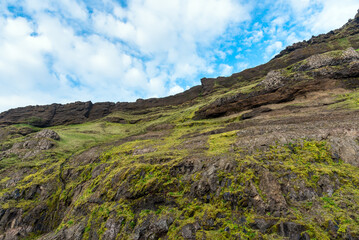 Fototapeta na wymiar Low angle view of a steep grassy cliff against blue sky with clouds in Iceland in summer. Natural background.
