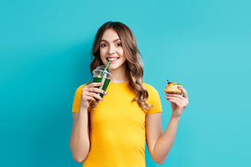 Happy young woman on dieting drinking detox juice holding cake in hand choosing healthy food