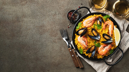 Traditional spanish seafood paella in pan with chickpeas, shrimps, mussels, squid on brown concrete...