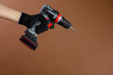 Female hands of a foreman in work gloves holds an electric screwdriver. Studio photography on a...