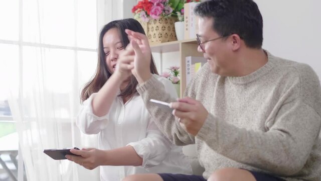 Excited young man and woman who are a couple playing together and competing in video games on smartphones, the man trying to bother his girlfriend on a sofa in the living room