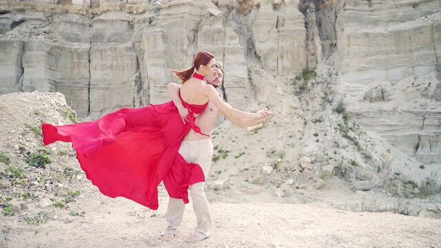 young Passionate loving couple of professional dancers dancing together on top of a mountain on nature outdoors. Man and woman in a red dress on a background of rocks and sand. romantic Modern ballet 