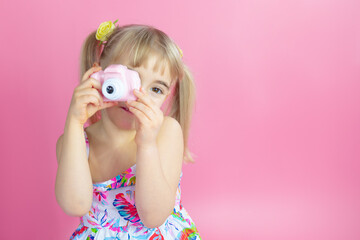 Cute smiling girl taking photo with pink toy digital camera.