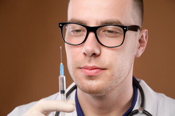 A young male Caucasian doctor in a glass holds a syringe with an injection with his gloved hand....