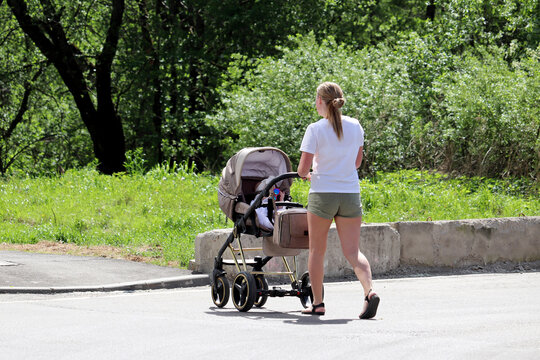 Woman in summer shorts with a baby stroller crossing the city street. Concept of motherhood, walking mom with pram