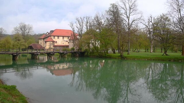 Otocec castle, the only water castle in Slovenia, located on an island in the middle of the Krka River. Famous wooden bridge over green water. Wide angle, left pan, real time