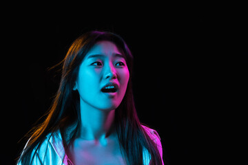 Fototapeta premium Asian young woman's portrait on dark studio background in neon. Concept of human emotions, facial expression, youth, sales, ad.