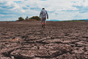 Obraz premium Man walking at cracked earth at the bottom dried up lake