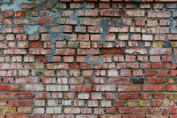 Old and broken brick, a sample of a brick wall in various shades of red, gray, orange and beige, sometimes covered with greenish mold. Wall texture and background for vintage wallpaper. 