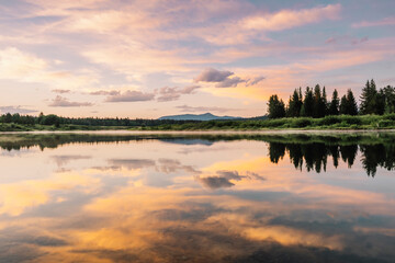 A gorgeous sunrise with an explosion of clouds and colors reflect off the waters of the Snake River in the Oxbow Bend area of Grand Teton National Park, Wyoming, USA. 