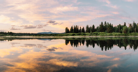 A panoramic photograph of a gorgeous sunrise with an explosion of clouds and colors reflect off the waters of the Snake River in the Oxbow Bend area of Grand Teton National Park, Wyoming, USA. 
