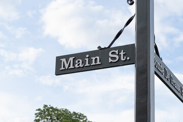 Wooden sign post with metal accents in a historical part of town showing Main Street with a cloudy sky and tree in the background.