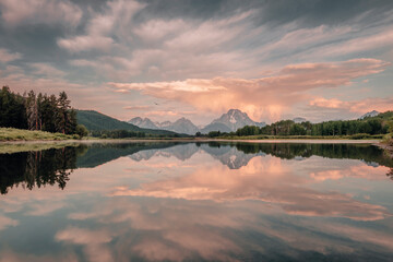 A pink anvil cloud rises above the Teton Range of the Rocky Mountains during a beautiful sunrise over the Snake River at Oxbow Bend in Grand Teton National Park, Wyoming, USA.