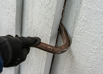 Crowbar held in hands while breaking down the wooden wall of a building being demolished.