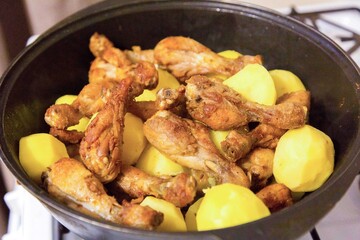 Chicken legs and potatoes are cooked in large saucepan.