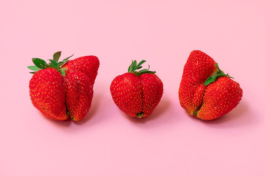 Large ugly strawberries on soft pink background. Ugly food concept