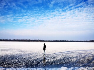  A silhouette of a lonely man in a dark coat stands on the ice of the river. Winter landscape photo
