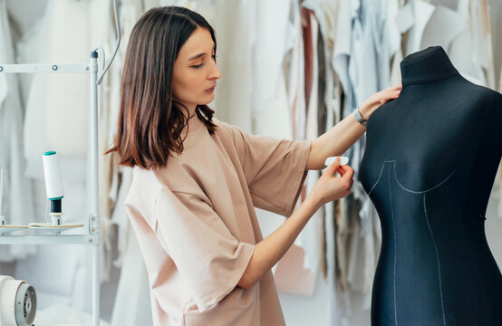 Side view shot of a fashion designer posing in her creative workshop. Young woman business owner working on the mannequin during preparing garment for a new collection in her creative office.