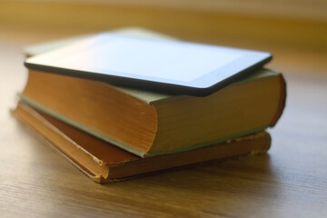 Stack of old hardcover books and e-reader on a table. Selective focus.