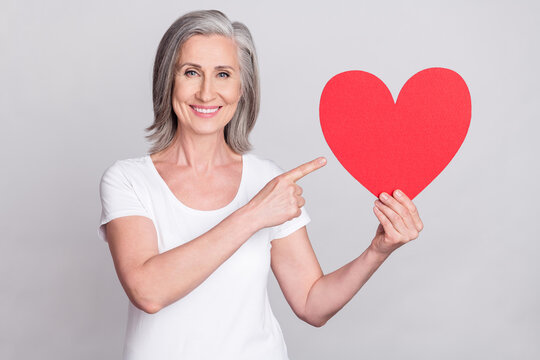 Photo of senior woman happy positive smile point finger heart advert choice select isolated over grey color background