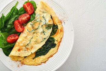 Omelet or omelette with spinach, cherry tomato and pepper seasoning on a white plate, on white background. Top view.